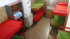 Un dormitorio con literas, un radiador y una estantería de madera con mantas.