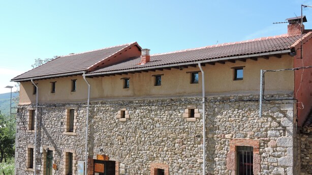 Un edificio de piedra con tejado de tejas, varias ventanas y una puerta pequeña.