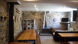 Un interior rústico con paredes de piedra, muebles de madera, una chimenea y un televisor montado en la pared.