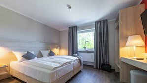 Una habitación de hotel moderna con una cama grande, mesitas de noche, un escritorio y una ventana con cortinas.