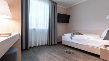 Camera d'albergo con scrivania in legno, un letto, una TV a parete e una finestra con tende.