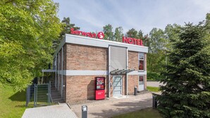 Un hotel con fachada de ladrillo, un letrero rojo y un pequeño quiosco en el exterior.