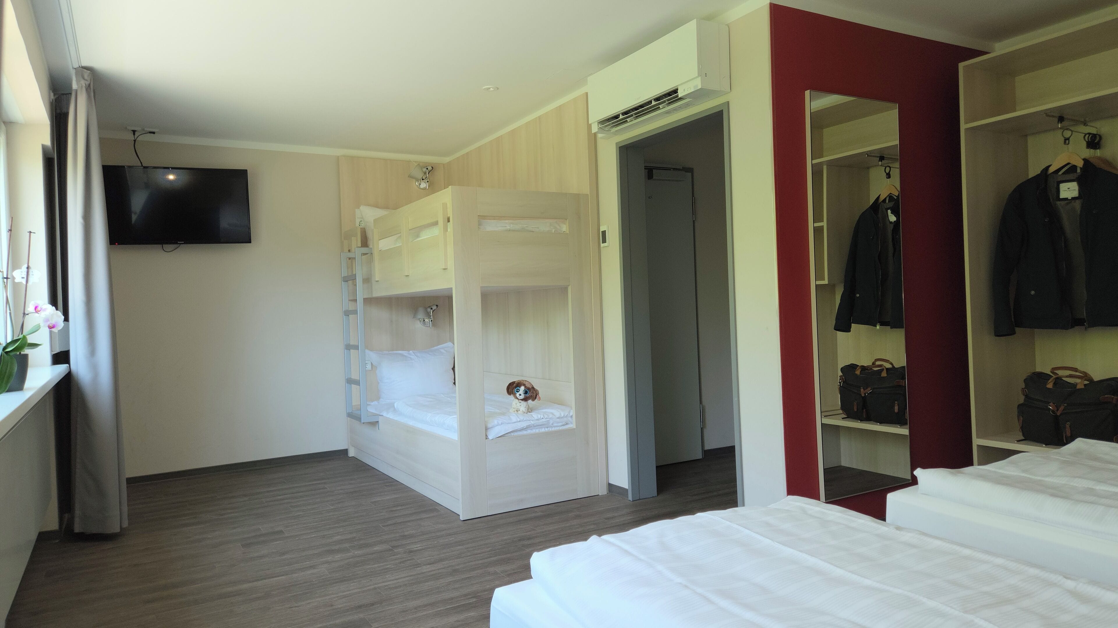 Una habitación de hotel compacta con literas, un armario y televisión en la pared.