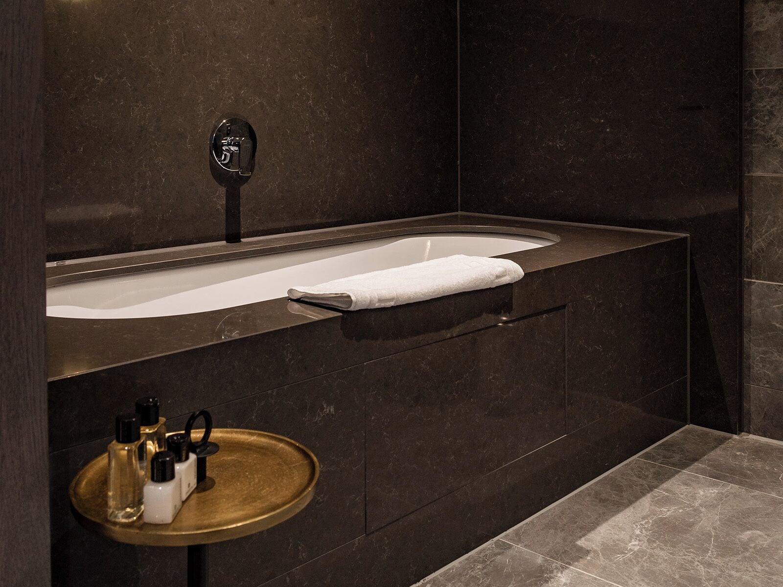 A modern bathroom with a freestanding bathtub, a vanity with a mirror, and a small round table with toiletries.