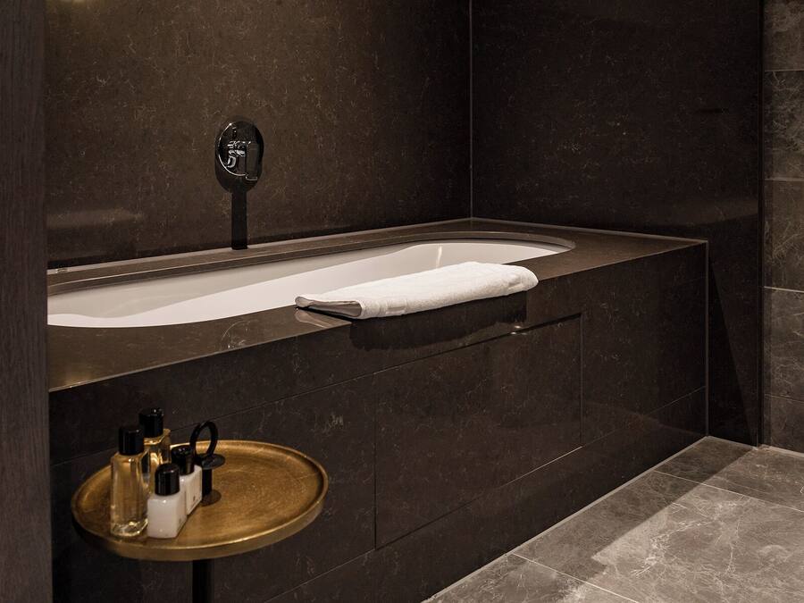 A modern bathroom with a freestanding bathtub, a vanity with a mirror, and a small round table with toiletries.