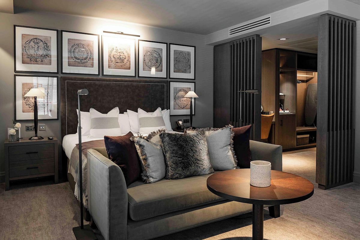 Et moderne hotelværelse med en seng, en sofa, et rundt sofabord og indrammet kunst på væggen.
