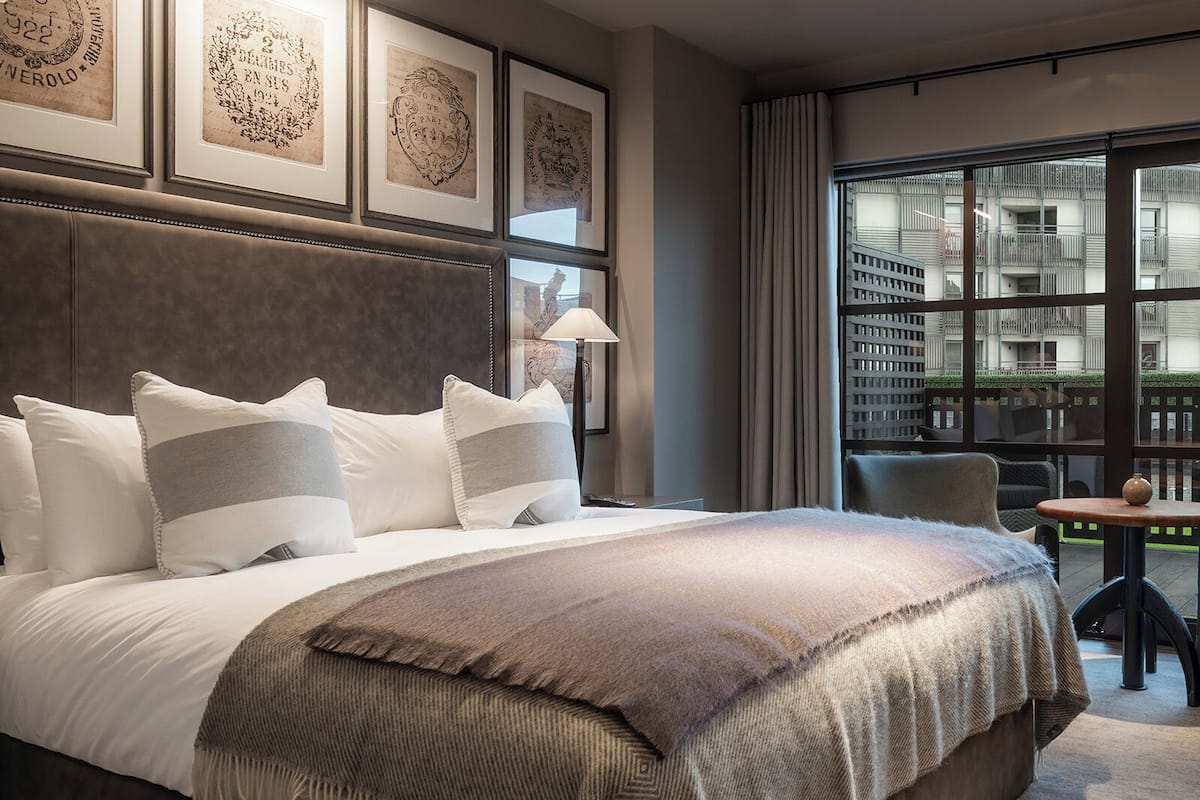 Et moderne hotelværelse med en stor seng, udsigt over byen gennem gulv til loft-vinduer og indrammet kunst på væggen.