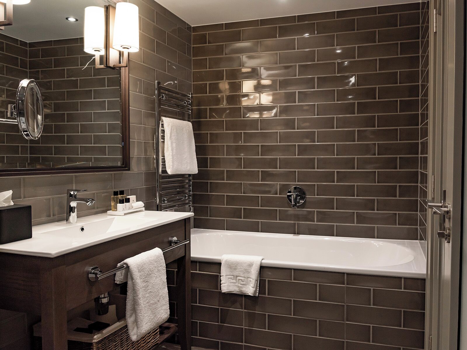 A modern bathroom with a dark brick wall, a white sink, a mirror, and a bathtub.