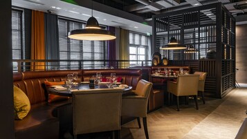 Un restaurante con cabinas de cuero, mesas redondas e iluminación colgante.