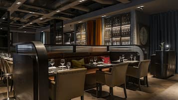 A restaurant with a modern interior, featuring a bar area with glassware on display, leather seating, and a clock on the wall.