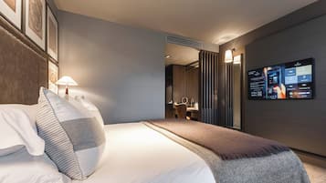 Quarto de hotel moderno com uma cama grande, uma escrivaninha e uma TV exibindo informações sobre o quarto.
