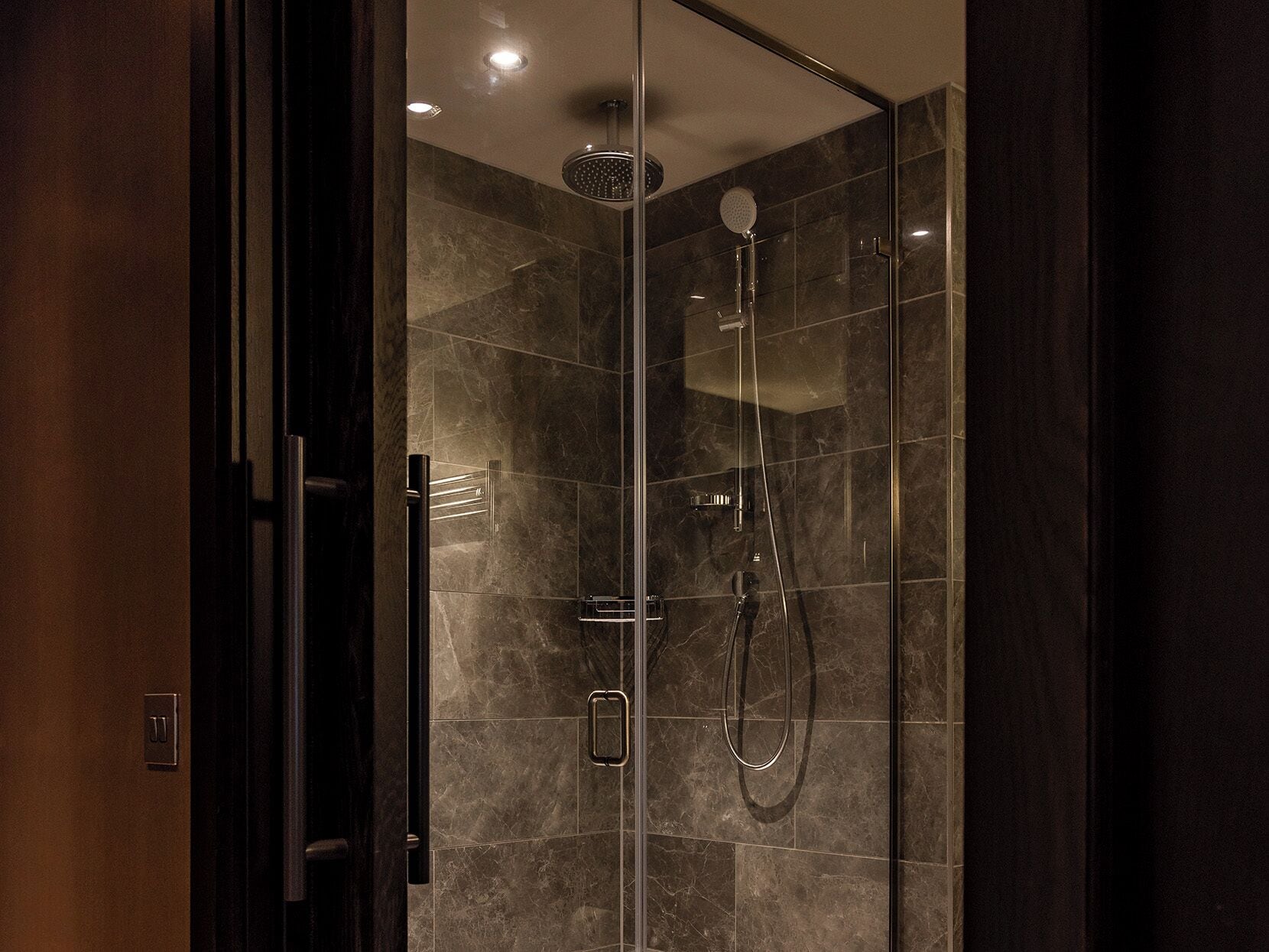 A modern shower with a handheld showerhead and a fixed rain showerhead, glass doors, and a control panel.