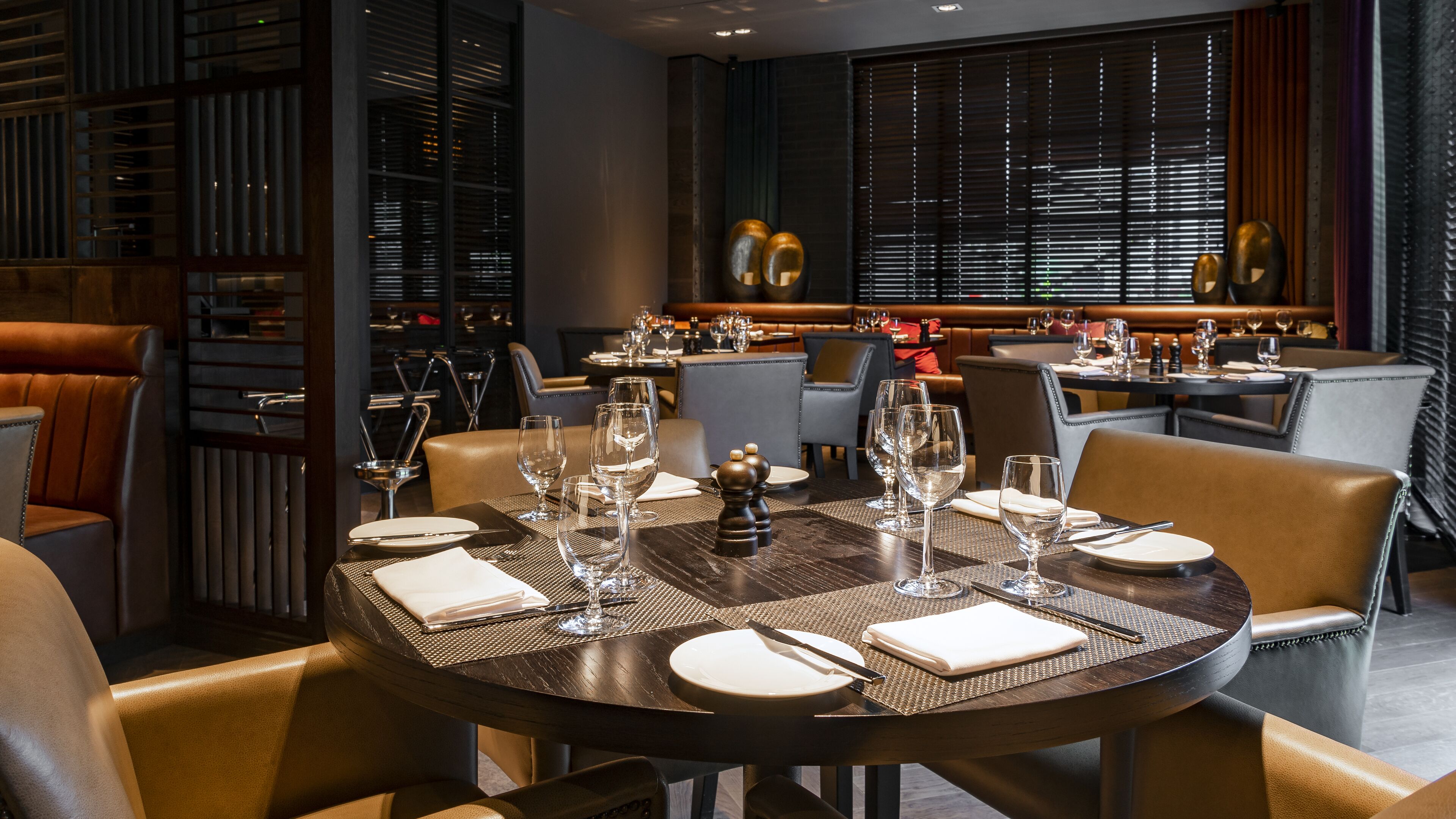 Restaurante com mesas redondas preparadas para refeições, apresentando copos e talheres.