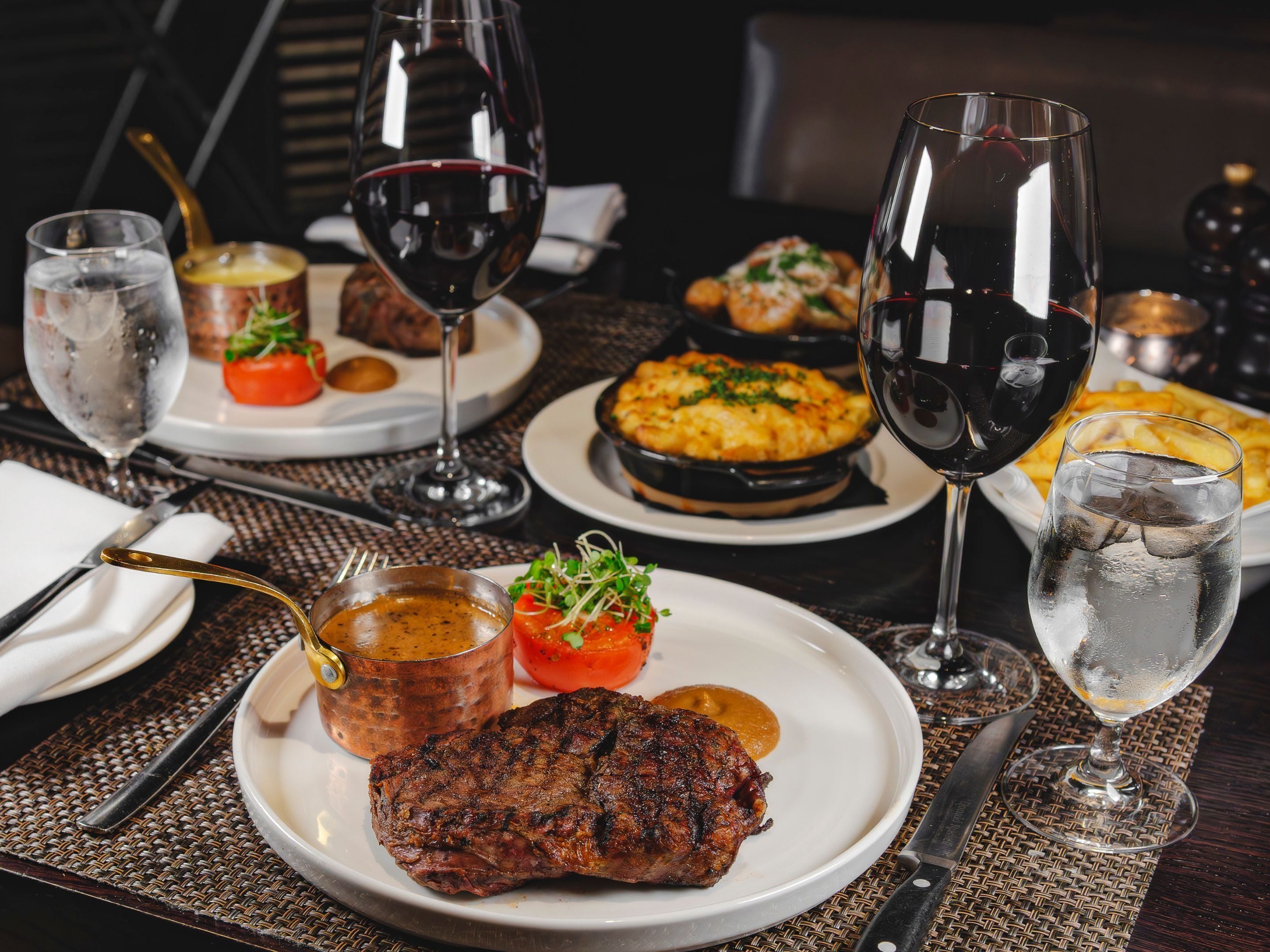 A dining table set with plates of food, glasses of wine, and cutlery.