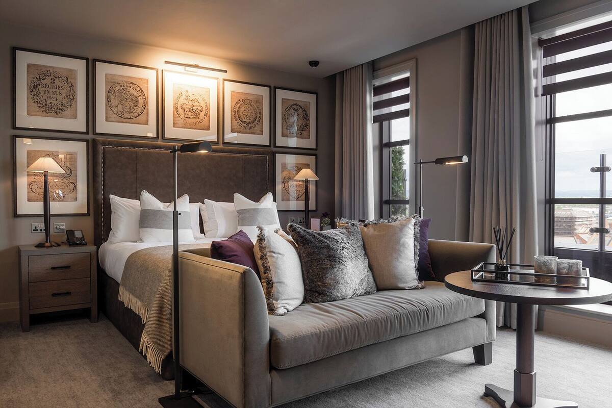 Et moderne hotelværelse med en stor seng, en sofa, et rundt bord og billeder i rammer på væggen.