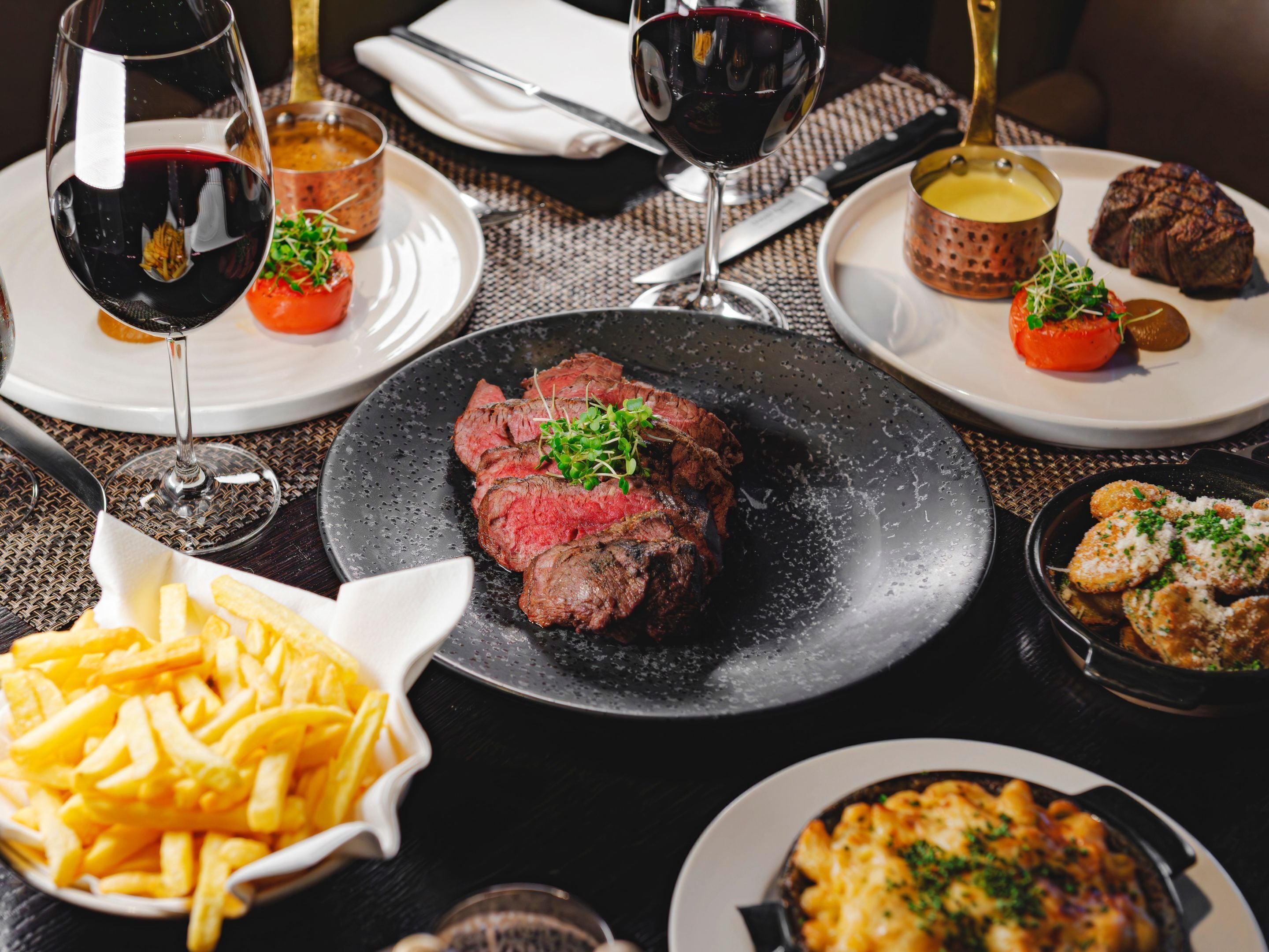 Una mesa de comedor con un bistec, papas fritas y diferentes bebidas.