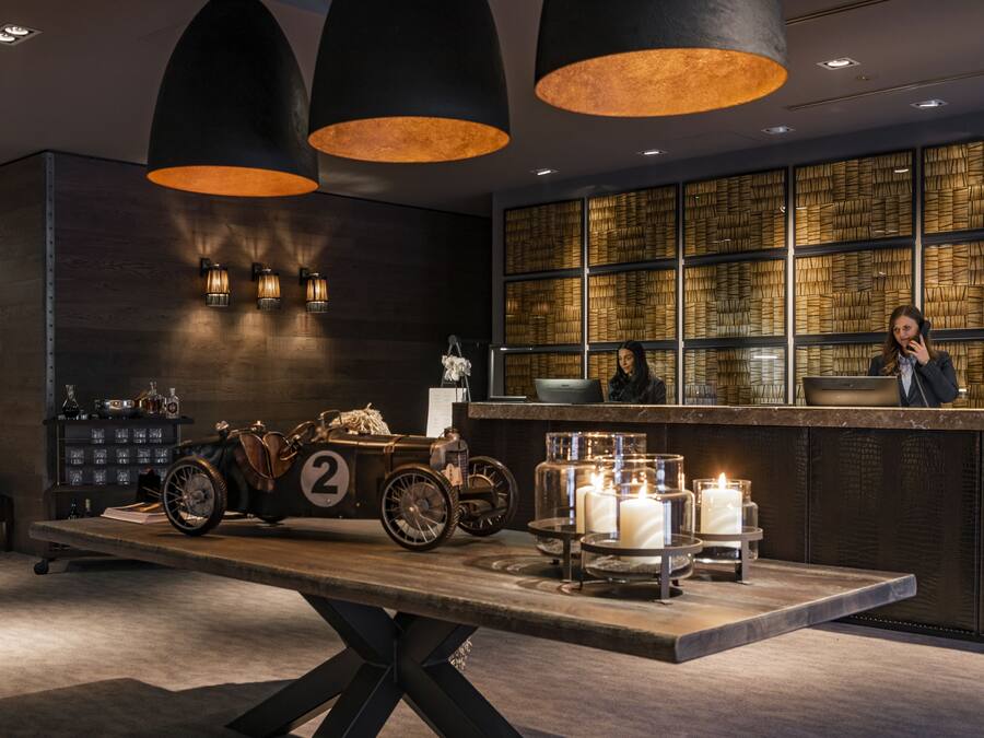 Zona de recepción con exhibición de un coche de carreras antiguo, mostrador con recepcionista y velas decorativas.