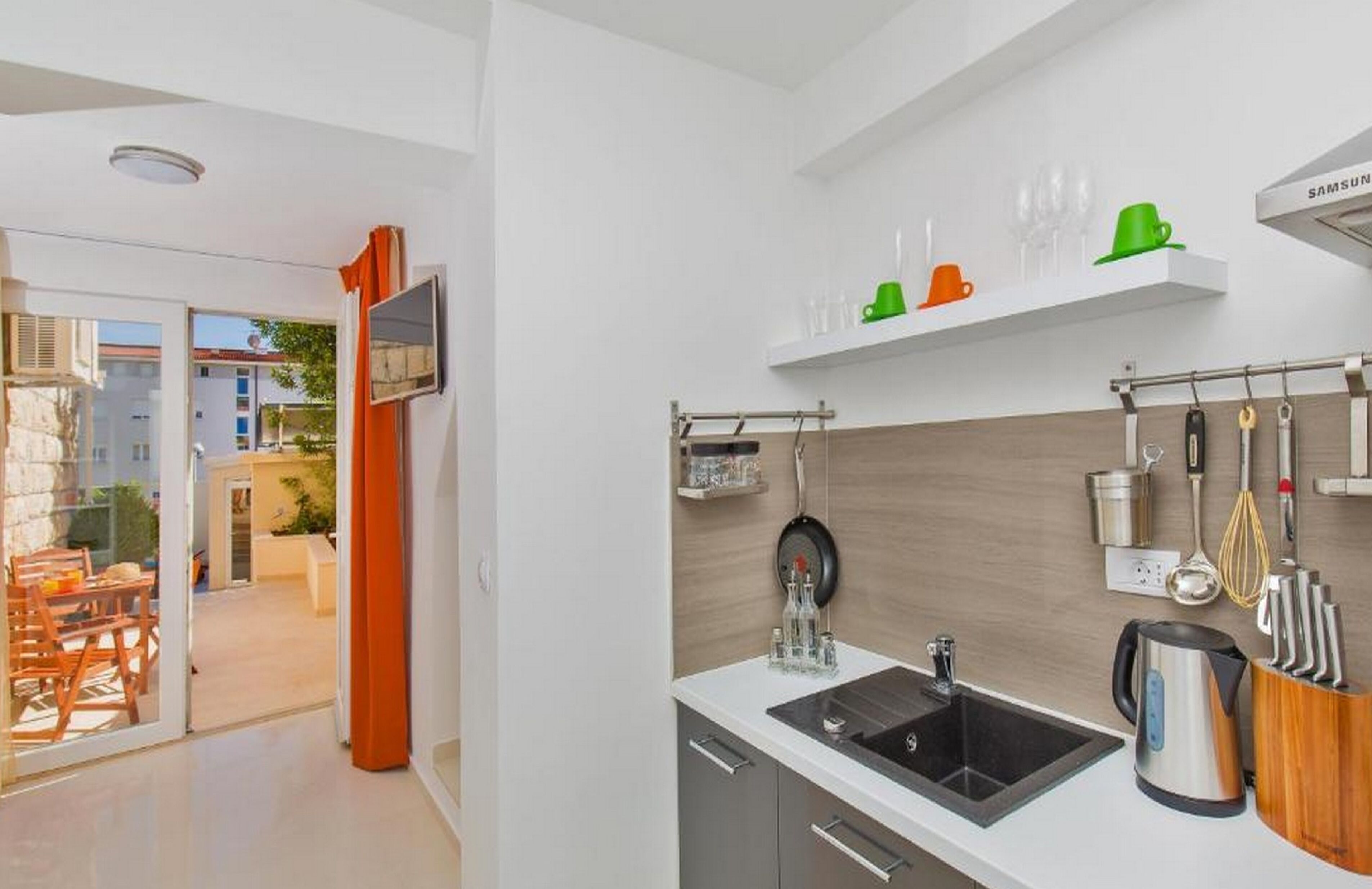 Una cocina moderna con un lavamanos negro, electrodomésticos de acero inoxidable y una encimera de madera. Se observan utensilios colgando y una cafetera.