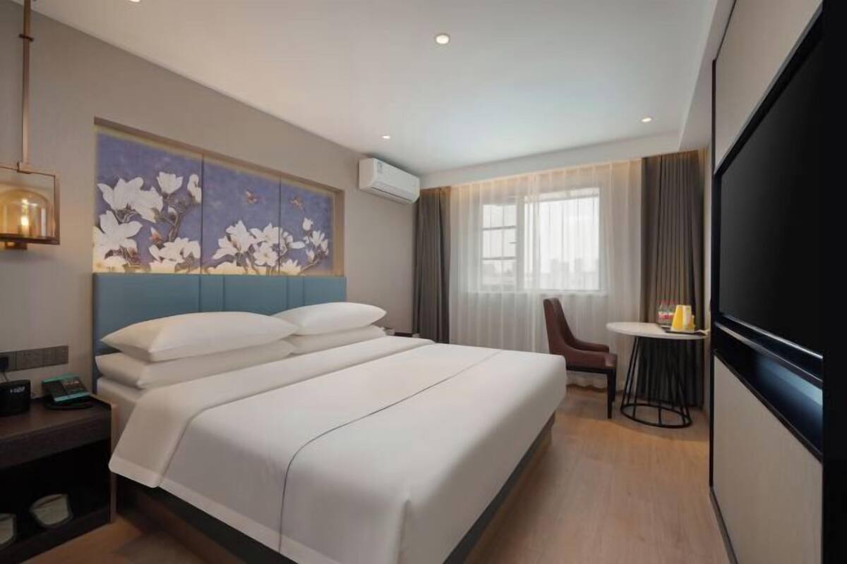 A hotel room with a large bed, a desk with a chair, a small table, and a large TV.