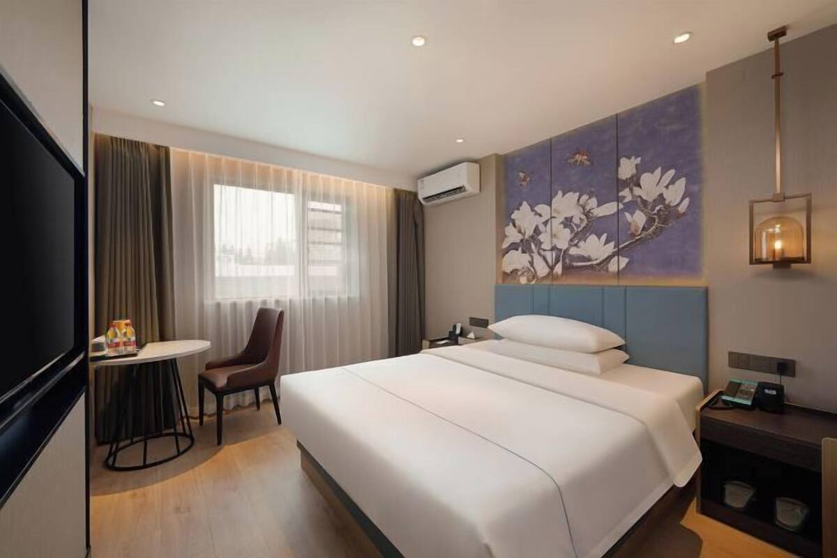 A hotel room with a bed, a desk with a chair, a television, and a painting on the wall.