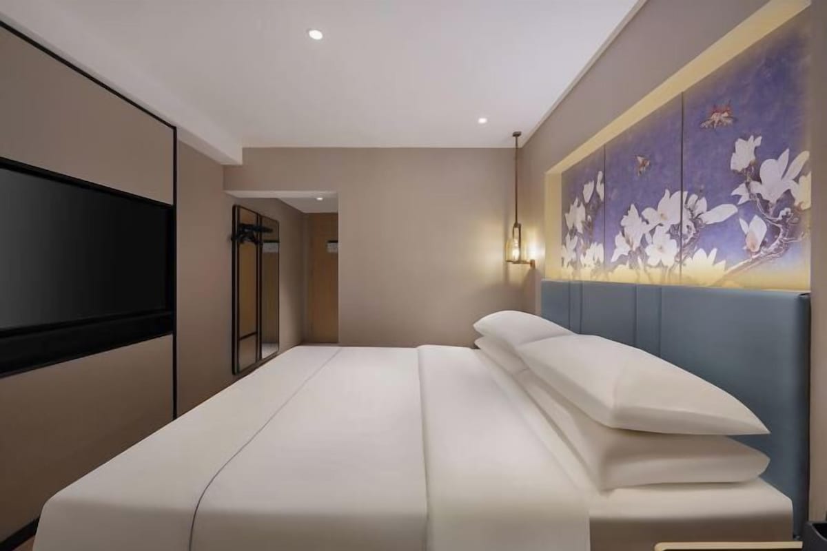 A hotel room with a bed, a TV, a wall-mounted artwork, and a door leading to a bathroom.