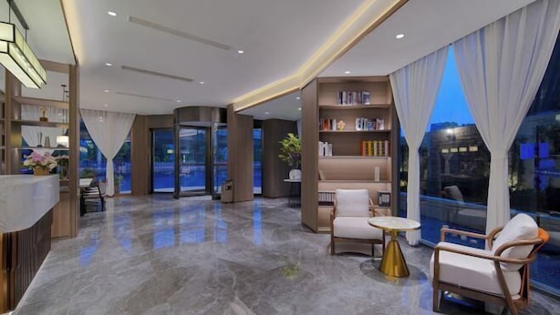 Un hall d’hôtel moderne avec un comptoir d’accueil, un espace salon et une grande fenêtre agrémentée de rideaux.
