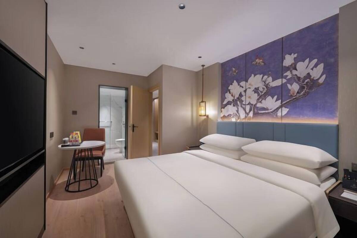 A hotel room with a large bed, a desk with a chair, a TV, and a painting on the wall.