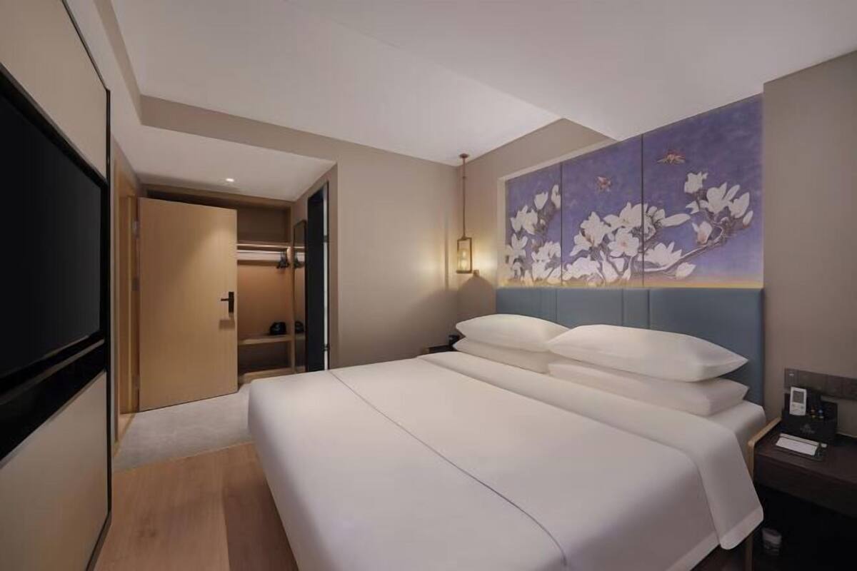 A hotel room with a large bed, a painting of flowers on the wall, a TV, and a desk with a lamp.
