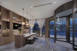 A modern hotel lobby with a marble floor, a central island with bar stools, and a large glass door leading outside. - Magnotel Hotel (Nanjing Hongshan Zoo Maigaoqiao Subway Station) (Nanjing)
