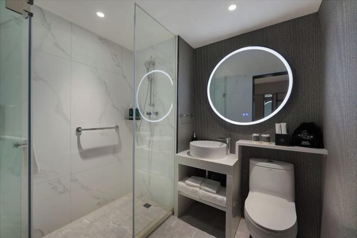 A modern bathroom with a glass-enclosed shower, a round mirror, a white sink, and a toilet.