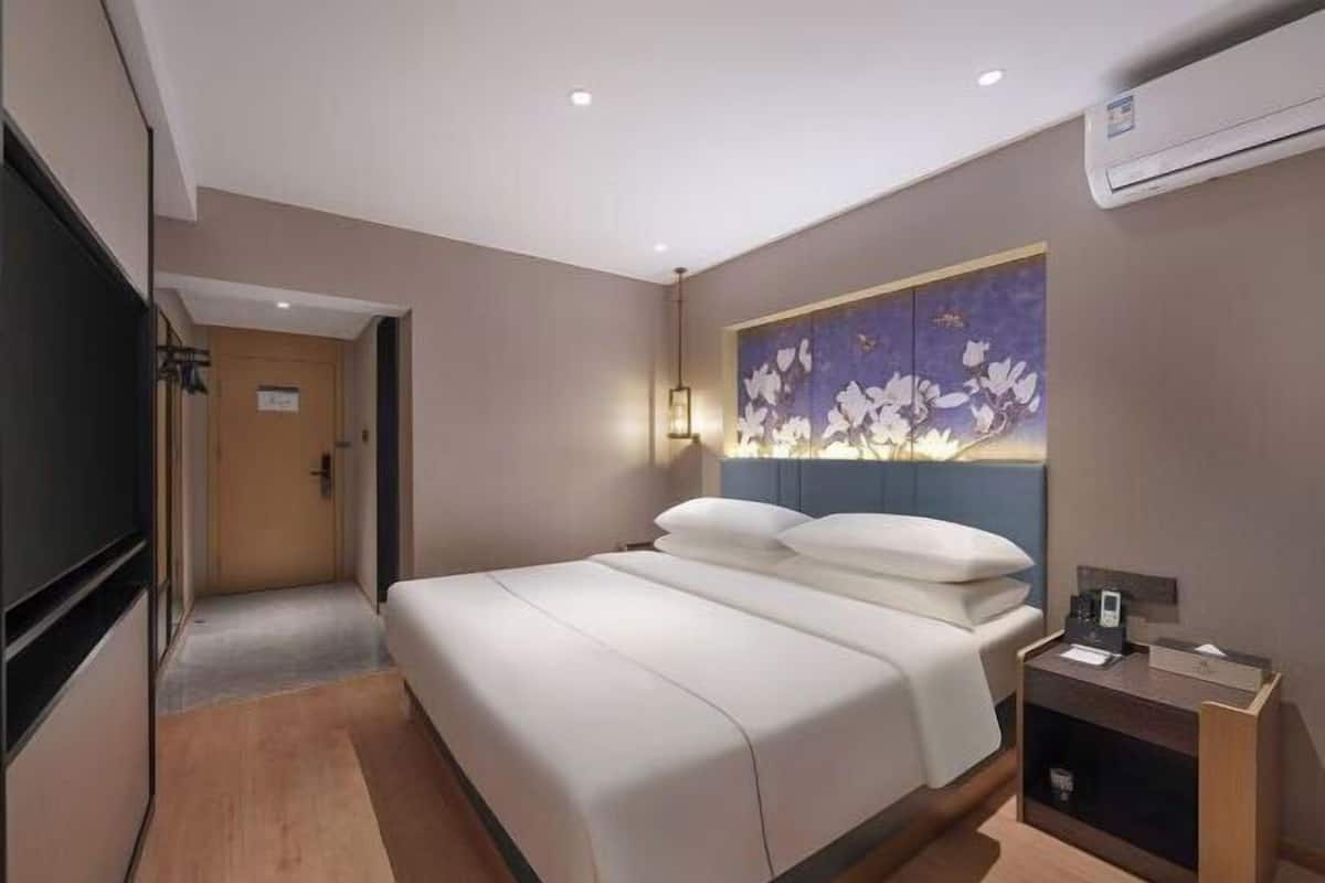 A modern hotel room with a large bed, a flat-screen TV, a bedside table, and a wall-mounted artwork.