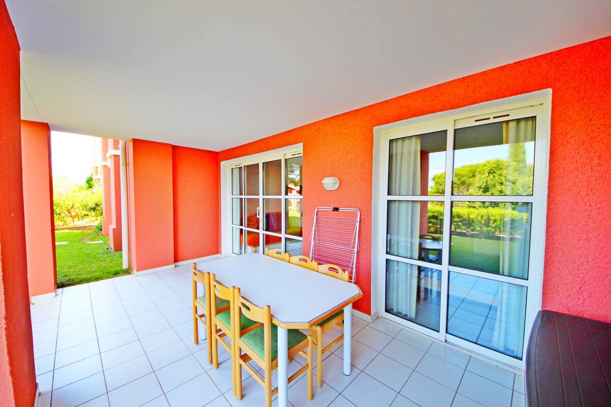 Une pièce lumineuse avec une table et des chaises blanches, de grandes fenêtres et un mur rouge.