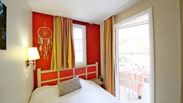 A bedroom with a bed, a nightstand, a lamp, a dreamcatcher, and a view of an outdoor patio with a table and chairs.