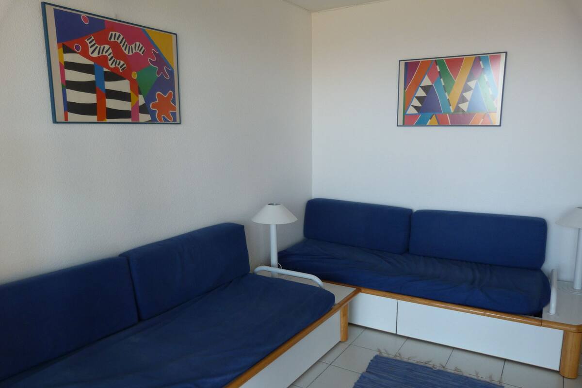 Un salon moderne avec un canapé bleu, une petite table d’appoint et deux tableaux accrochés au mur.