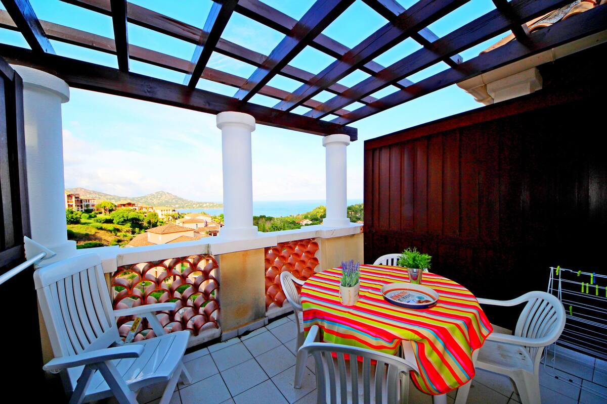 Une terrasse couverte avec des chaises blanches et une table, une vue sur la mer et une pergola en bois.