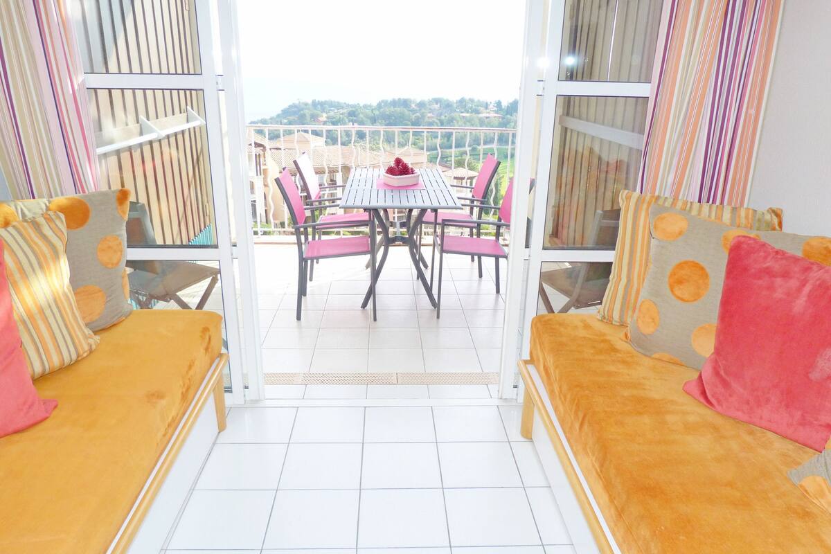 Un balcon avec une table et des chaises, un canapé et une vue sur une colline.