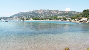 Eine Küstenlandschaft mit klarem, flachem Wasser, einem steinigen Strand und einem gebirgigen Hintergrund.