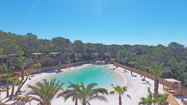 A beach resort with a large pool, palm trees, and beach chairs. - La Pierre Verte Camping Village (Fréjus)