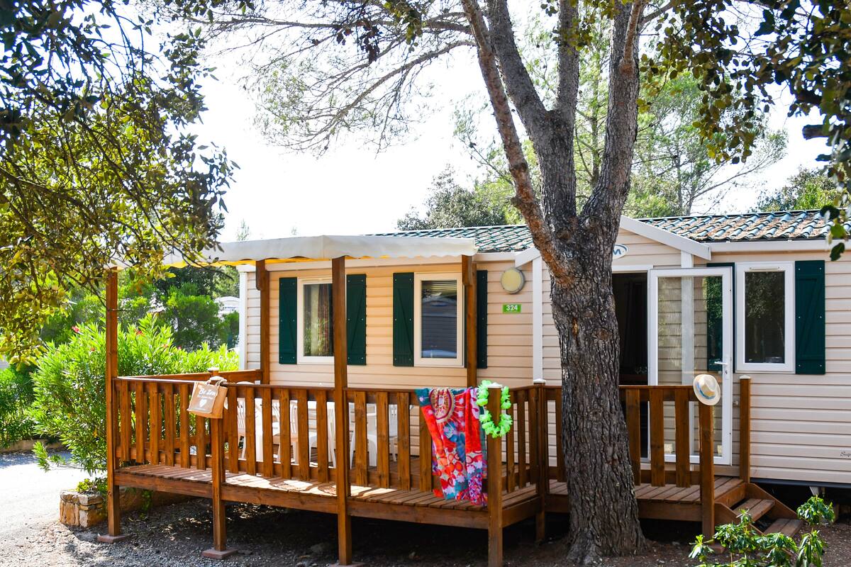A wooden deck with a bench and a small table, a tree, and a mobile home with a number '324' on the side.
