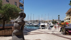A marina with boats docked, a statue, and a pedestrian walkway. - La Pierre Verte Camping Village (Fréjus)