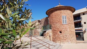 A stone tower with a cross on top, a staircase leading up to it, and a building with balconies in the background. - La Pierre Verte Camping Village (Fréjus)