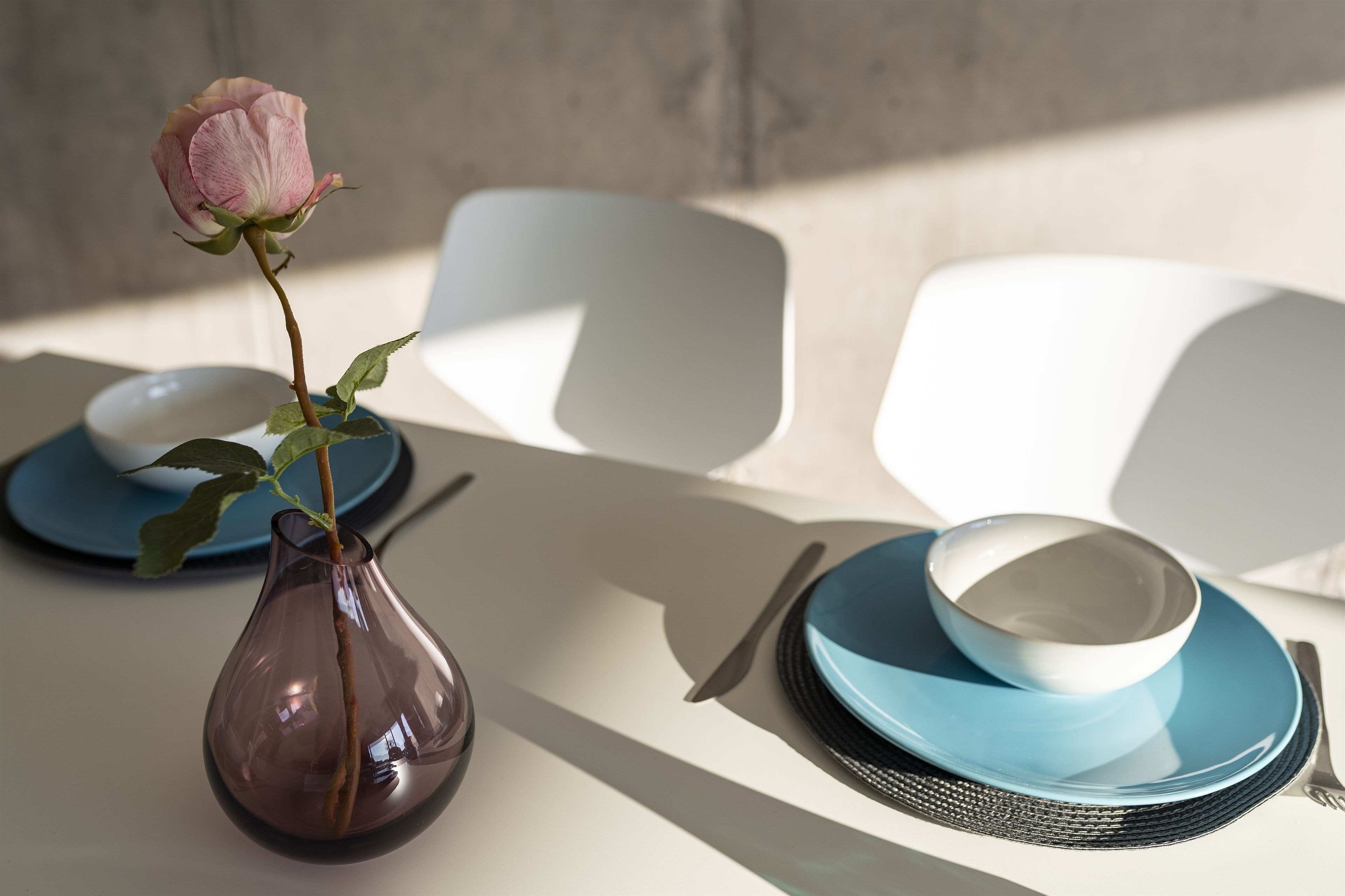 A dining table with a vase of a single rose, a bowl, and plates.