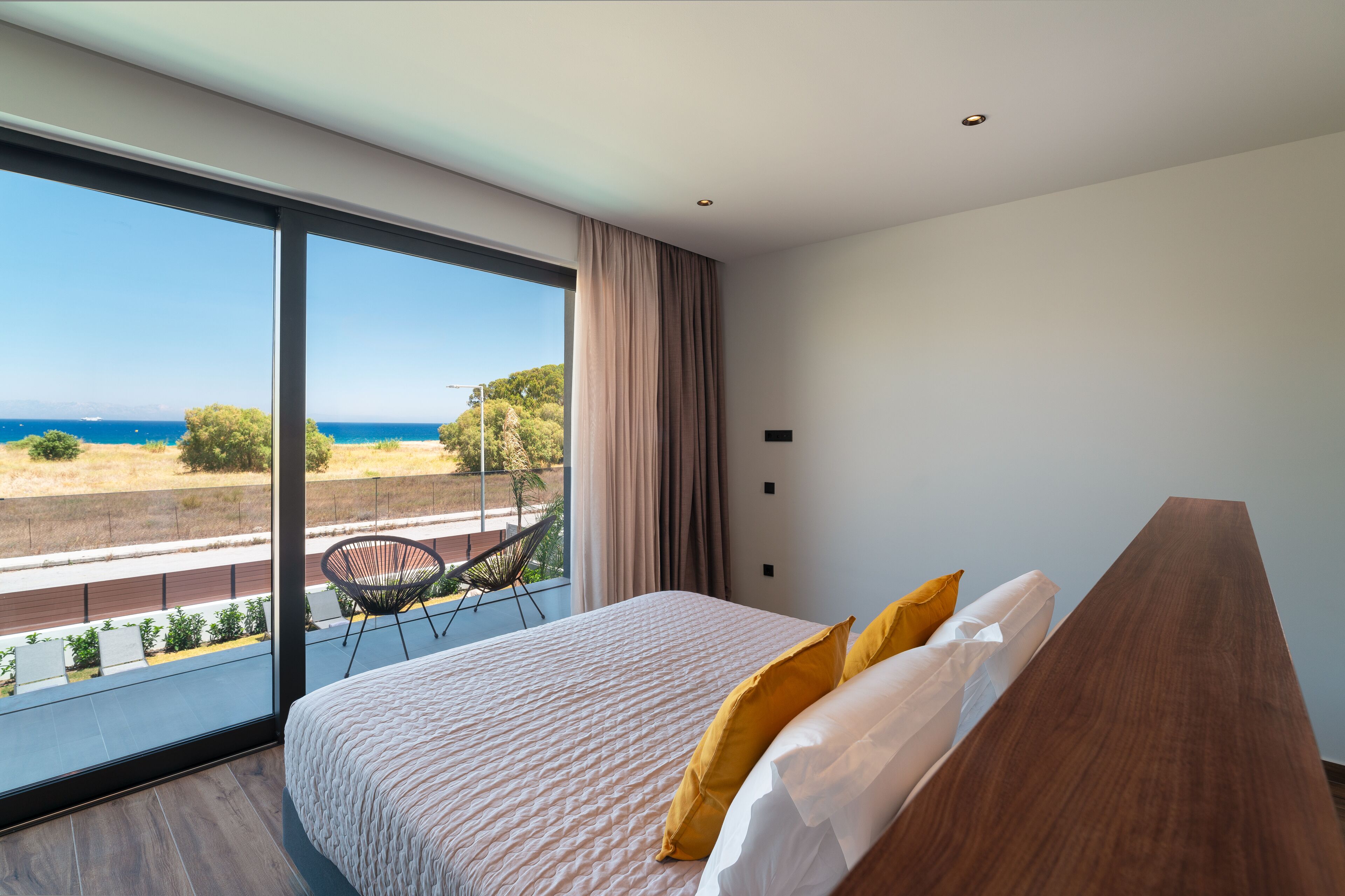 A bedroom with a large bed, a view of the sea, and a balcony with a chair.