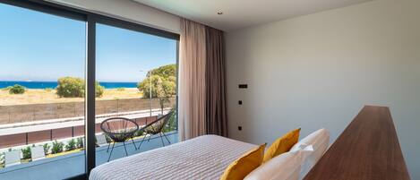 A bedroom with a large bed, a view of the sea, and a balcony with a chair.