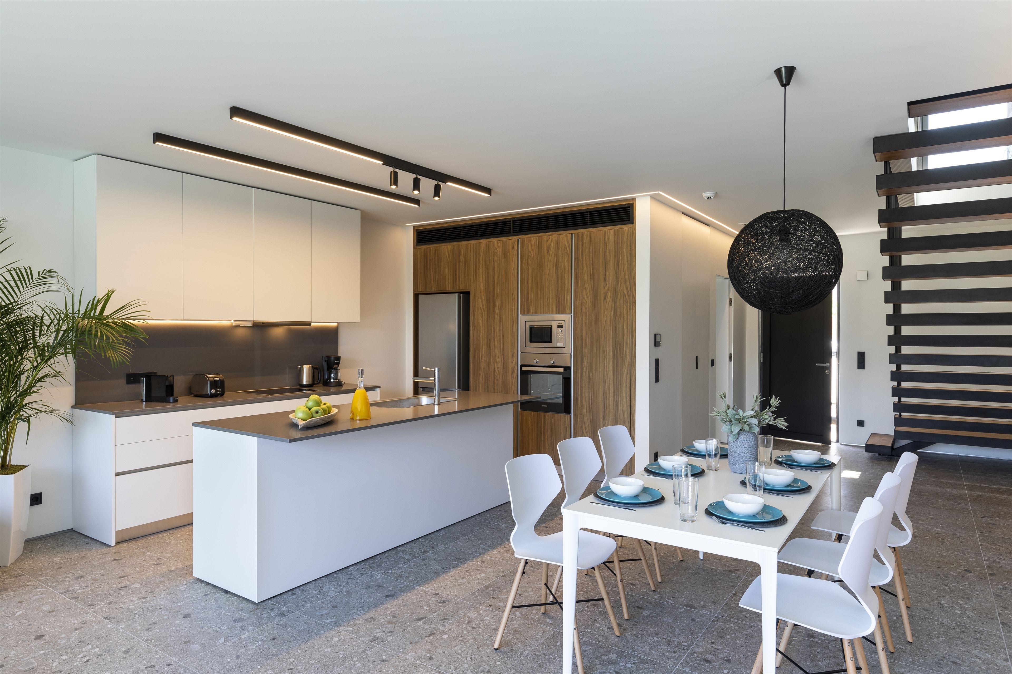 A modern kitchen with a central island, built-in appliances, and a dining area with white chairs and a table set for six.
