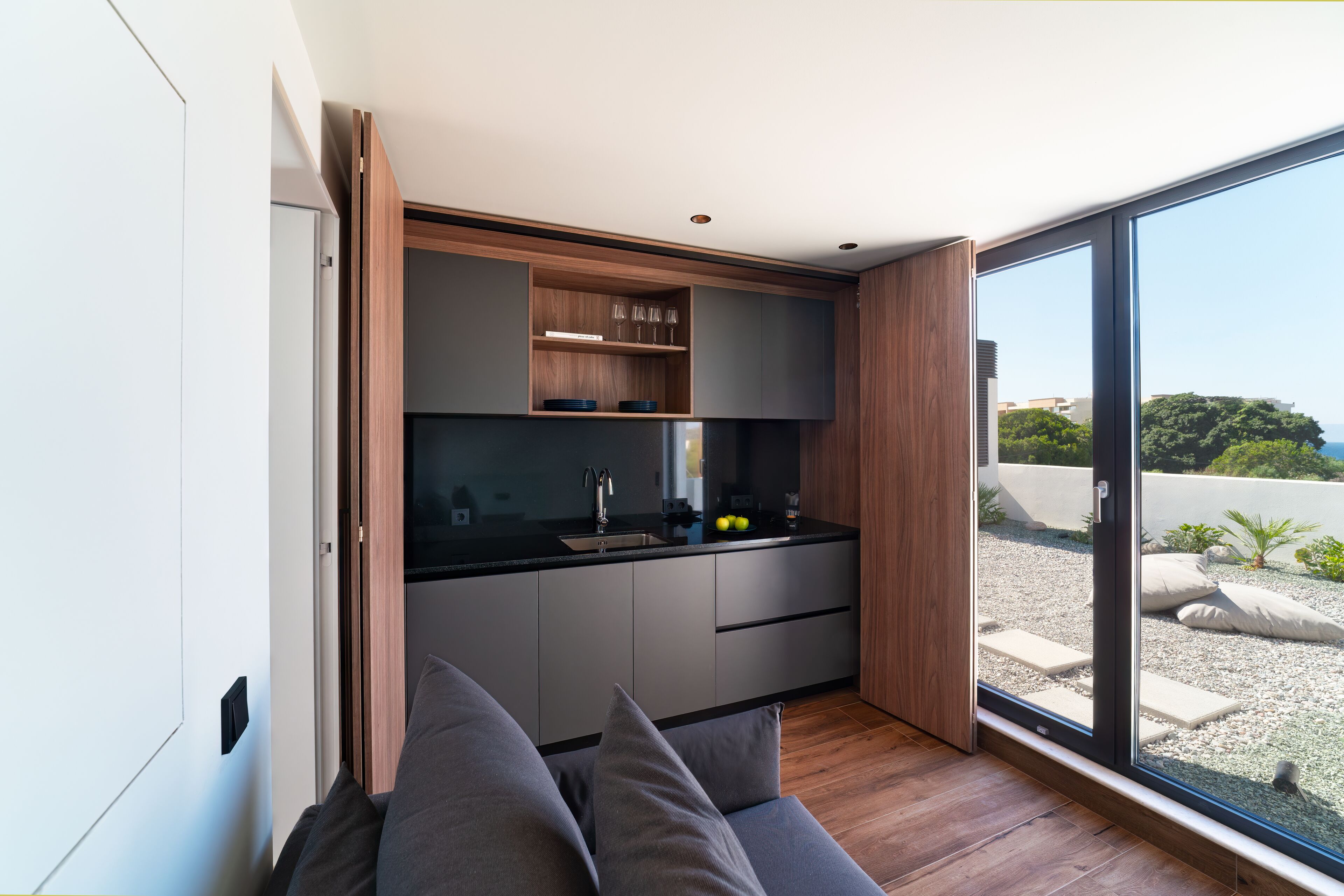 A modern kitchen with a built-in oven, a sink, and a window overlooking a garden.