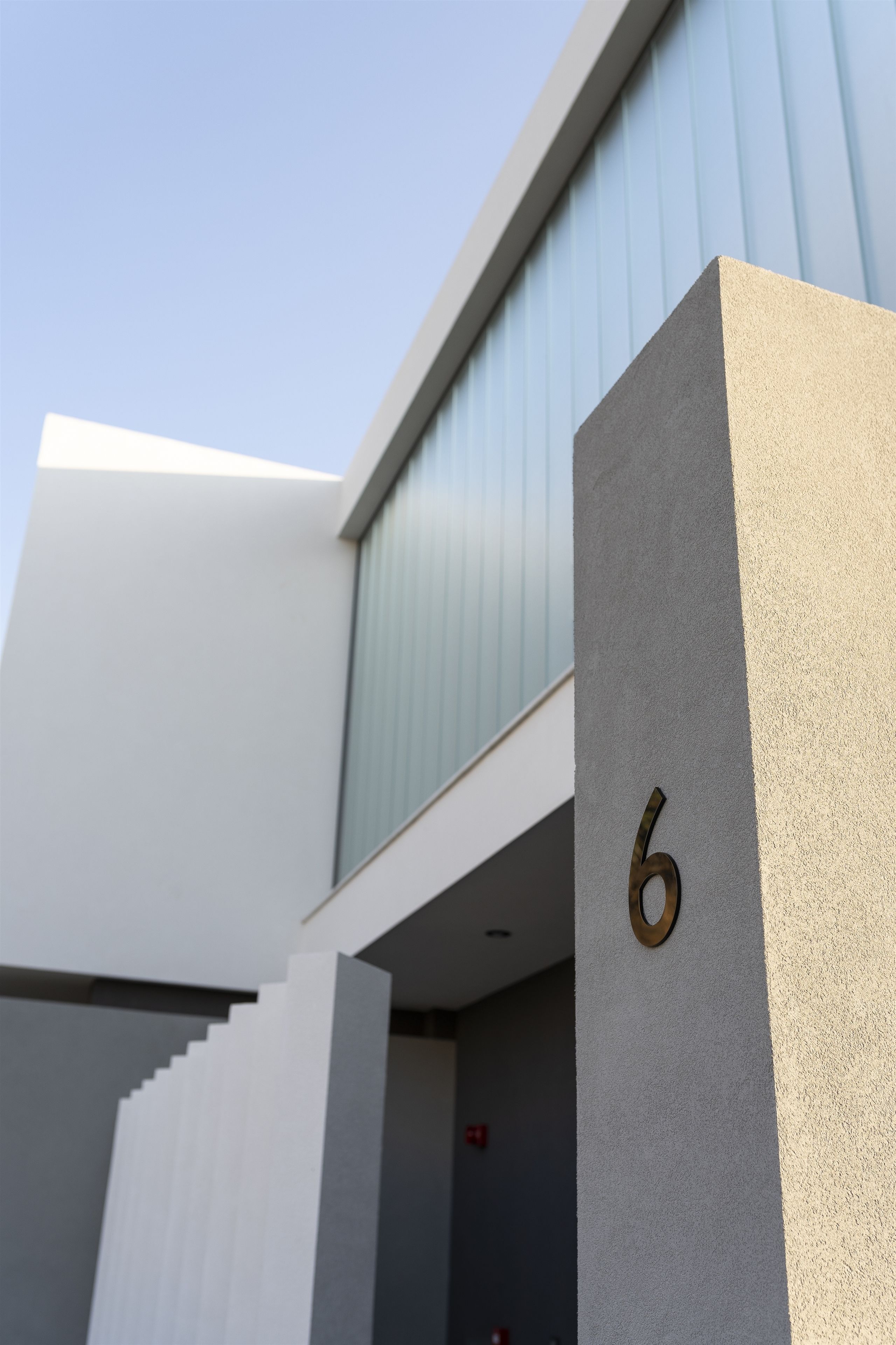 Un edificio moderno con techo plano, un ventanal grande y el número 6 destacado en una pared con textura.