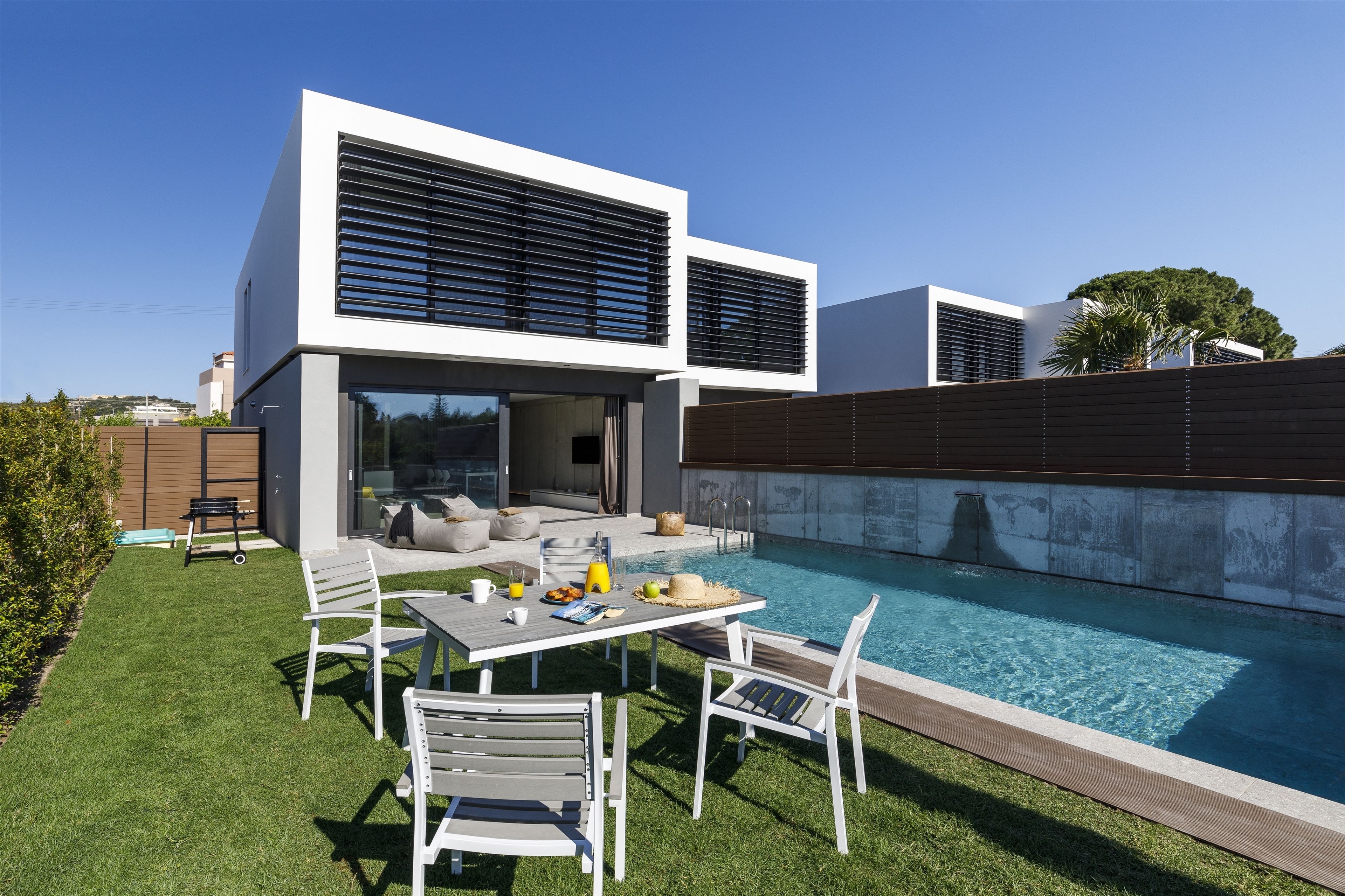 A modern house with a swimming pool, outdoor seating, and a large window overlooking the pool.