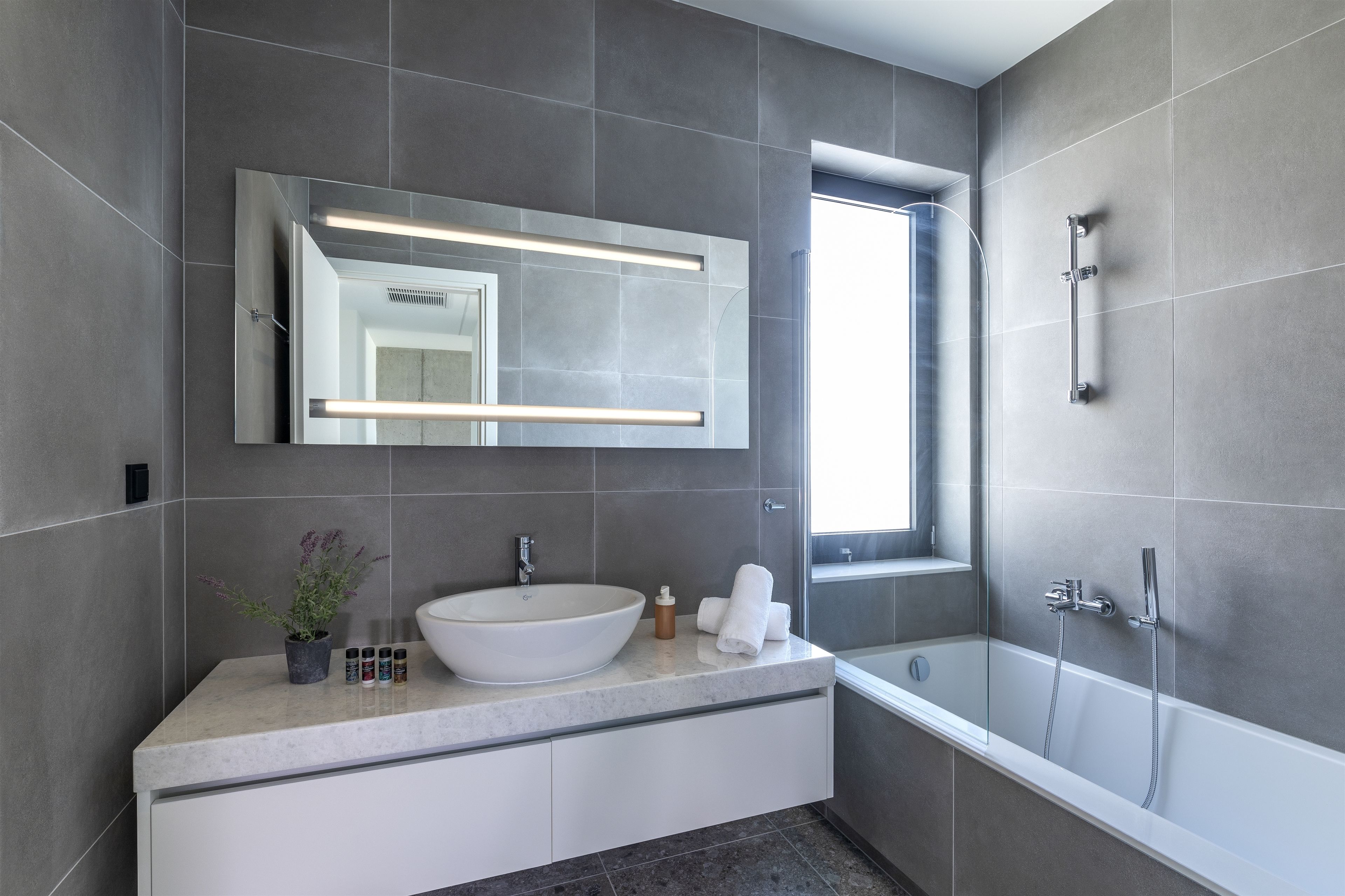 Une salle de bain moderne avec un grand miroir, un lavabo sur colonne, une douche et une fenêtre.
