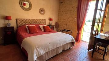Cozy retreat with a large bed, stone wall, and terracotta floor, featuring a modern pendant light and a small dining area.